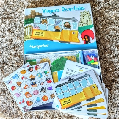 Jogo Viagens Divertidas com autocarro amarelo, cartas ilustradas e marcadores coloridos sobre tapete castanho