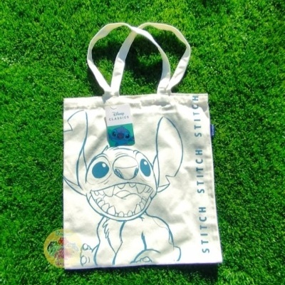 Saco de tecido branco com desenho azul do Stitch da Disney sobre relva verde