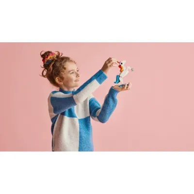 Menina sorridente a brincar com figura de unicórnio de peças de encaixe em fundo rosa