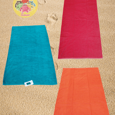 Três toalhas retangulares coloridas sobre areia.