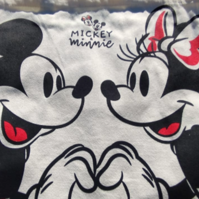 Mala de pano branca com estampa de Mickey e Minnie, mãos juntas em forma de coração, em relva verde.