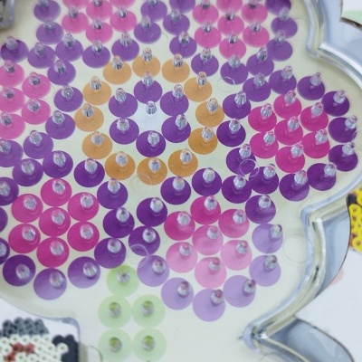 Placa em forma de flor com pequenos pinos coloridos para montagem de padrões