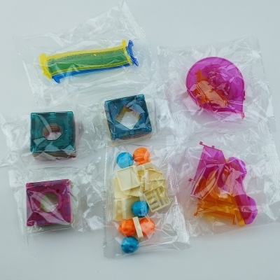 Brinquedos plásticos coloridos embalados individualmente em sacos transparentes sobre superfície branca