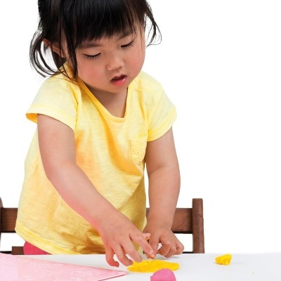 Criança asiática a brincar com massa de modelar amarela e rosa numa mesa branca