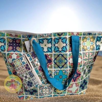 Saco de praia com padrão de azulejos coloridos e alças azuis na areia junto ao mar