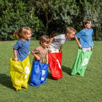 Crianças a correr em sacos coloridos numerados no relvado