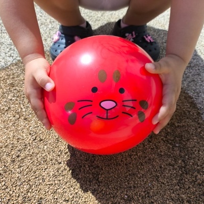 Bola vermelha com rosto de gato nas mãos de uma criança em chão texturizado