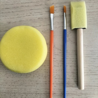 Conjunto de pincéis e esponjas de pintura amarelas e cabos coloridos sobre madeira clara