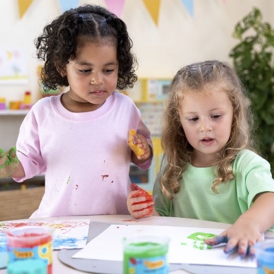 Duas crianças a pintar com as mãos em papéis brancos com tintas coloridas