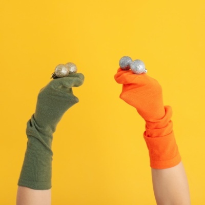 Duas mãos com luvas verdes e laranja seguram bolas decorativas douradas e prateadas