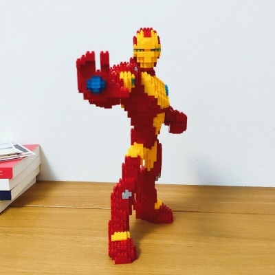 Figura Iron Man feita de blocos de montar vermelhos e amarelos numa mesa de madeira.