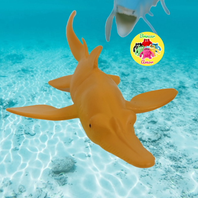 Brinquedo tubarão amarelo em água clara com fundo areia branca