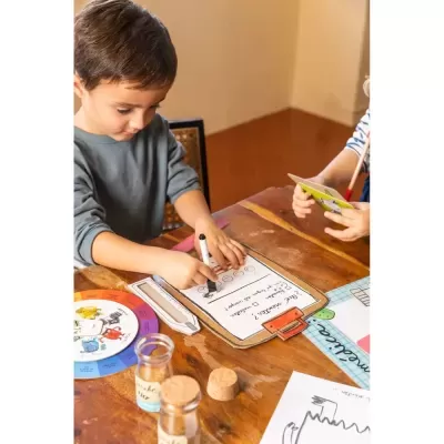 Criança a escrever numa prancha de madeira numa mesa com material educativo e frascos