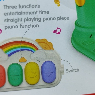 Brinquedo musical infantil com botões coloridos e arco-íris em plástico branco e texto em inglês sobre funções