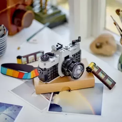 câmara fotográfica de brinquedos feita de blocos de construção sobre base de cartão e fotografias numa mesa branca