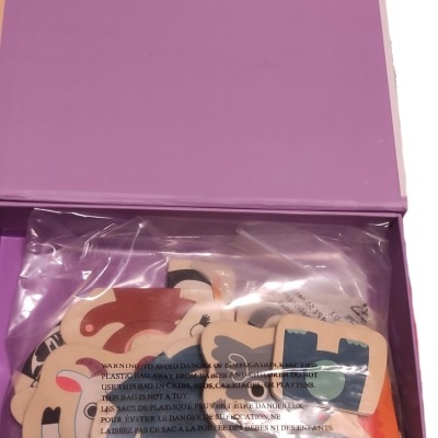 Caixa roxa aberta com peças ilustradas coloridas dentro de saco plástico