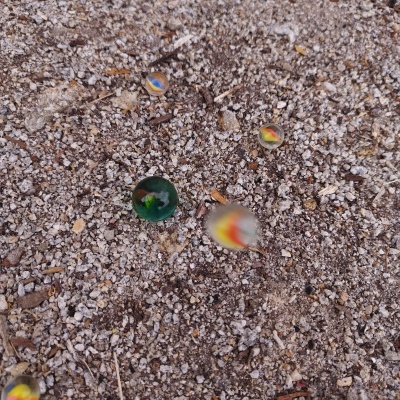 Bolinhas de vidro coloridas sobre um solo arenoso com pequenas pedras.