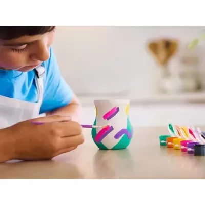 Criança pintando vaso de cerâmica colorido numa mesa