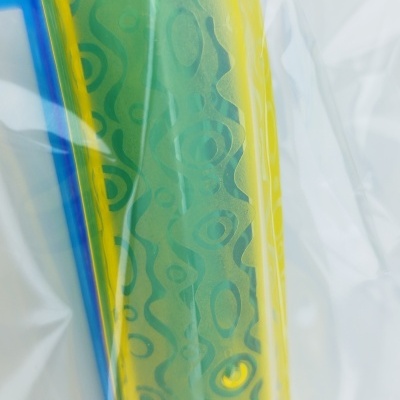 Cartucho de impressora amarelo e azul com padrões verdes dentro de saco plástico