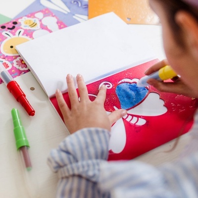 Criança a colorir desenho de borboleta com marcador azul e máscara vermelha
