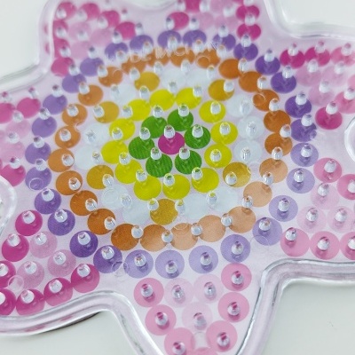 Base plástica transparente em forma de flor com pequenos pinos coloridos em padrão concêntrico