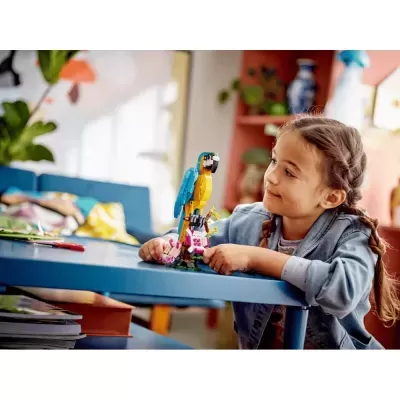 Criança a brincar com brinquedo de papagaio feito de blocos de construção sobre mesa azul