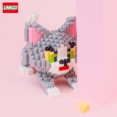 Miniatura de gato cinzento feita de blocos tipo LEGO com olhos verdes e amarelos junto a lasca de queijo amarela