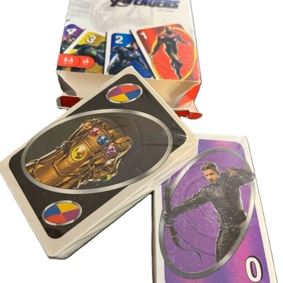 Cartas do jogo UNO edição Avengers com caixa e duas cartas em destaque, uma com Manopla do Infinito e outra com personagem roxo número 0