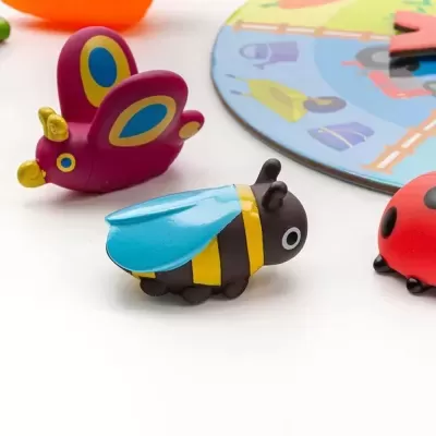 Brinquedos de insetos coloridos de plástico sobre superfície branca e tabuleiro de jogo