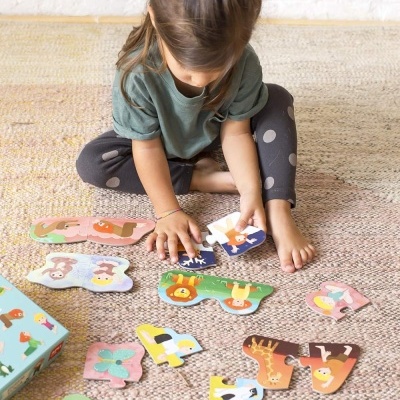 Menina a montar puzzle colorido de animais e crianças sobre tapete claro