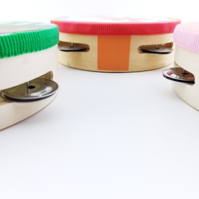 Três pandeiros de madeira com fitas coloridas e pratos metálicos sobre superfície branca