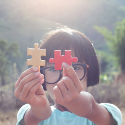 Criança a mostrar peças de puzzle castanha e vermelha ao ar livre