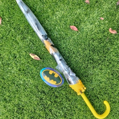 Guarda-chuva fechado com cabo amarelo e padrão do Batman sobre relva