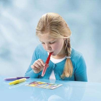 Garoto com camisola azul clara usando tubo vermelho para assobiar numa mesa branca com tubos coloridos e cartão