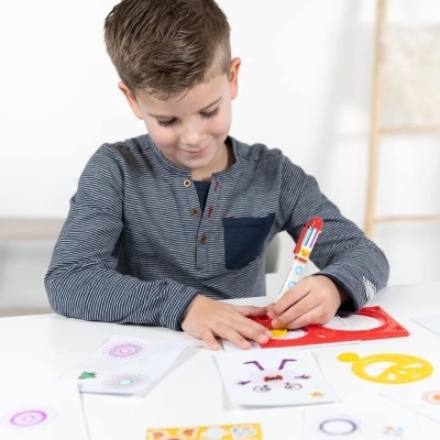 Criança a desenhar com caneta multicolor numa mesa com estêncil vermelho e desenhos coloridos