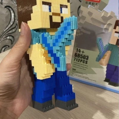 Figura de blocos tipo LEGO segurando objeto azul com caixa ao fundo