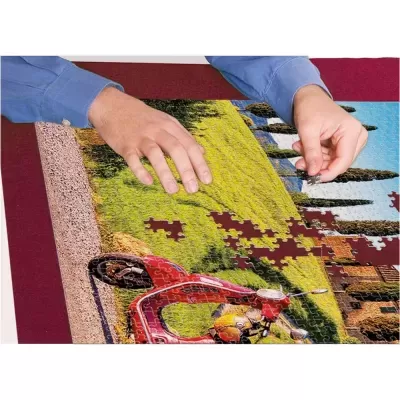 Puzzle com imagem de scooter vermelha em campo verde sendo montado em mesa com tabuleiro vermelho