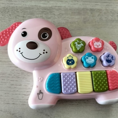 Brinquedo musical infantil em forma de cão cor de rosa com botões coloridos e teclas texturizadas