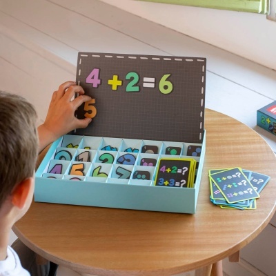 Jogo educativo com peças magnéticas de números coloridos e sinais matemáticos numa caixa azul clara