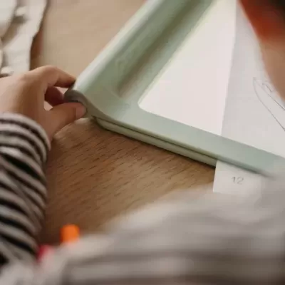 Criança a mexer num quadro branco com moldura verde clara sobre mesa de madeira