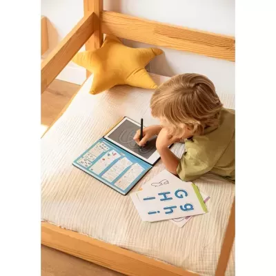 Criança a desenhar num tablet num colchão branco com almofada estrela amarela e cartões educativos