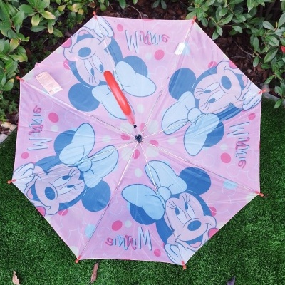Guarda-chuva infantil rosa com estampas da Minnie aberto sobre relva artificial.