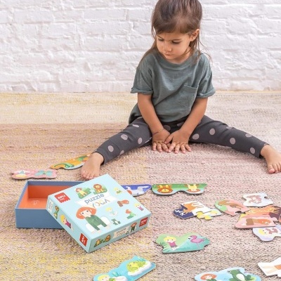 Criança a jogar puzzle de madeira com animais e pessoas, caixa azul com texto Puzzle Yoga e Apli Kids