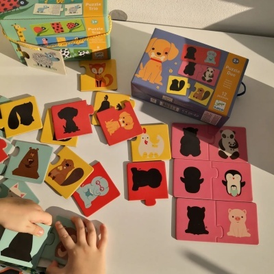 Conjunto de puzzles infantis coloridos com animais, embalagem rotulada 'Puzzle Duo 2+' e mãos de criança a brincar.
