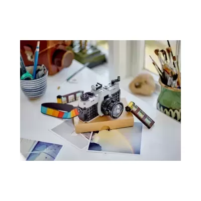Câmera de brinquedo feita de blocos de construção em cima de mesa com fotografias e pincéis próximos à janela