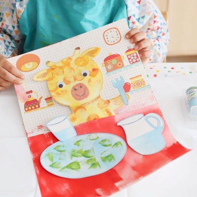 Livro infantil com girafa e pratos coloridos na mesa