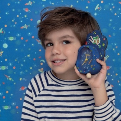 Menino com camiseta riscada e despertador azul com padrão espacial