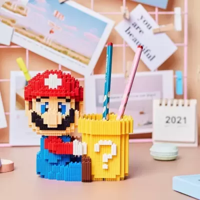 Porta-lápis estilo Lego com personagem Mario e bloco de interrogação amarelo contendo lápis em secretária decorada.