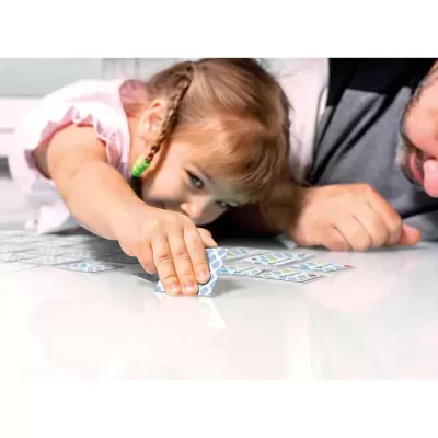 Menina a jogar cartas com padrão azul e branco numa mesa branca
