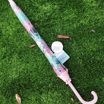 Guarda-chuva colorido fechado com cabo rosa e etiqueta Disney sobre relva